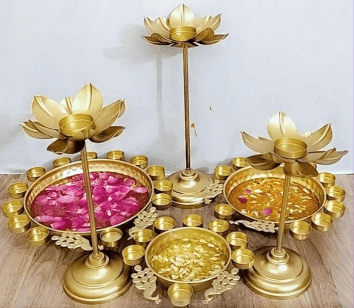 Three brass lotus candle holders with bowls of colorful petals, surrounded by small candles in a decorative arrangement.